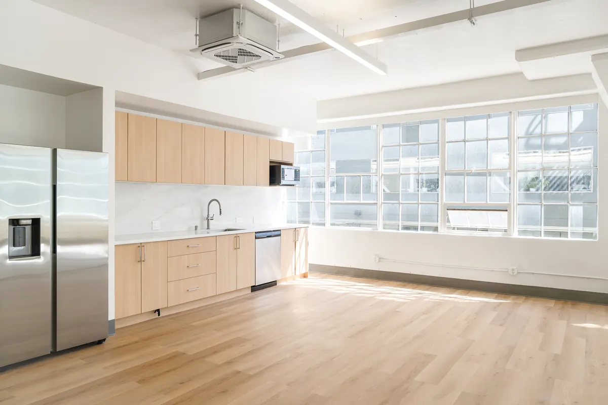 Kitchenette with light wood casework, stainless appliances and steel-framed windows